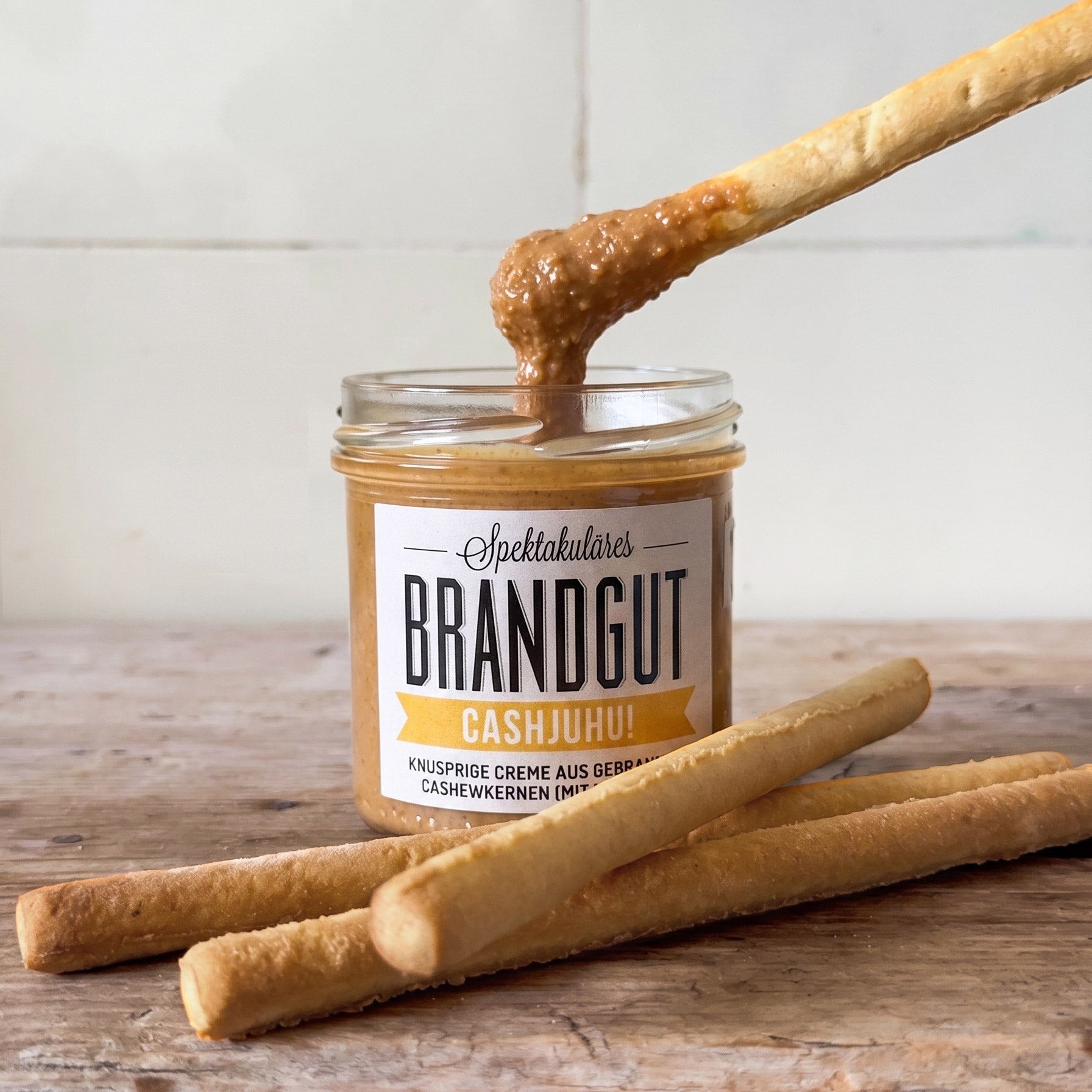 Ein Glas "Brandgut" Cashewcreme "Cashjuhu" auf Holz, Grissini, Cracker, Nussdip