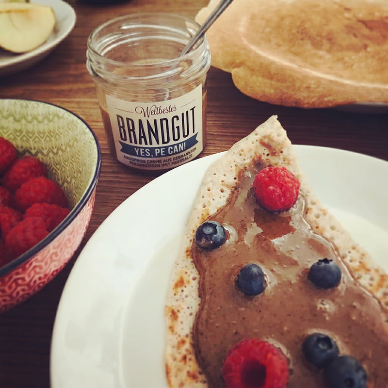 Pfannkuchen mit Nusscreme und Obst auf einem Frühstückstisch, 1 Glas "Brandgut" "yes, pe can".