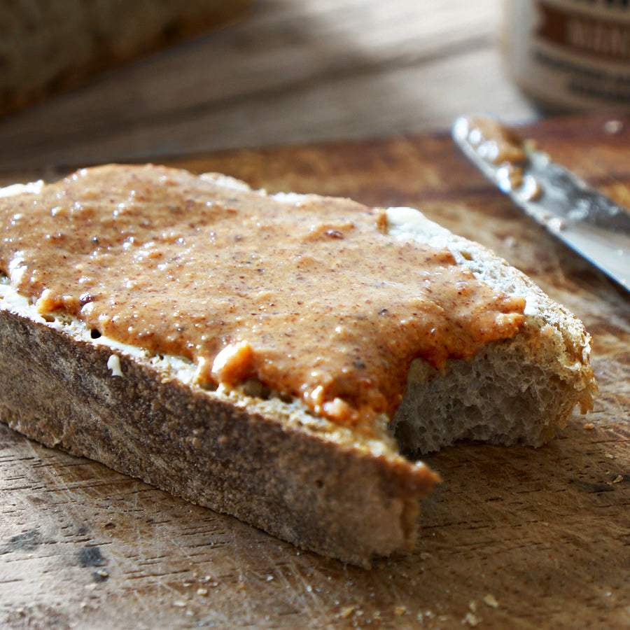 Angebissene Scheibe Brot mit Mandelcreme "Mandelikat" von BRANDGUT auf Holzbrett
